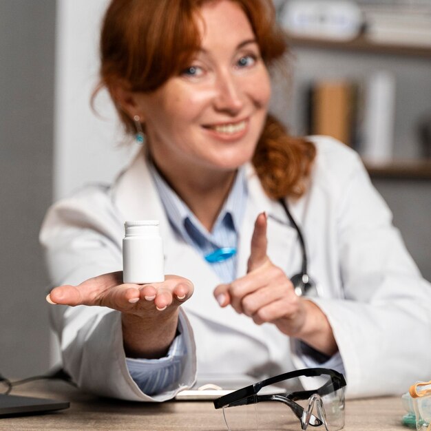 Vista frontal de uma sorridente médica oferecendo um frasco de remédio