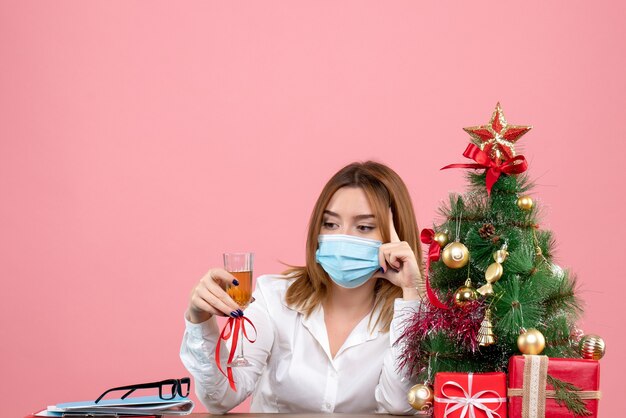 Vista frontal de uma trabalhadora com máscara estéril comemorando o natal com champanhe em rosa