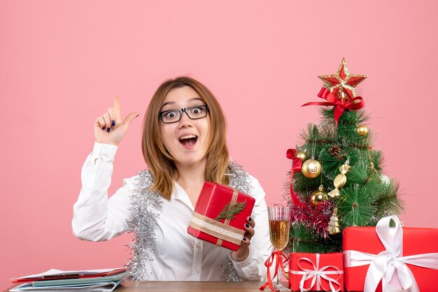 Vista frontal de uma trabalhadora sentada ao redor de presentes de Natal e árvore na rosa