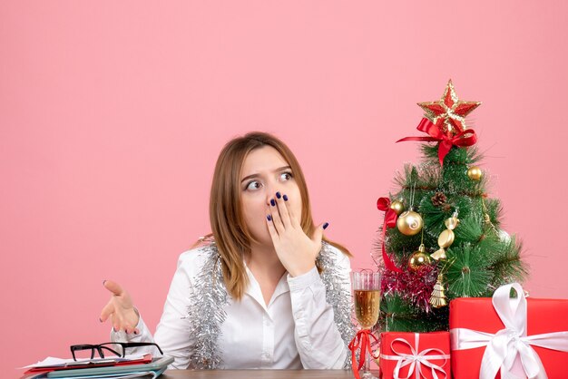 Vista frontal de uma trabalhadora sentada ao redor de presentes de Natal na rosa