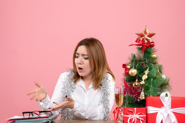Vista frontal de uma trabalhadora sentada ao redor de presentes de Natal na rosa
