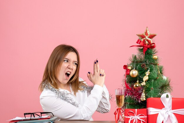 Vista frontal de uma trabalhadora sentada ao redor de presentes de Natal posando em rosa
