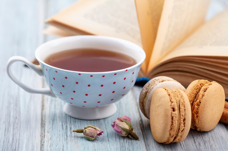 Foto grátis vista frontal de uma xícara de chá com macarons e um livro aberto em uma superfície cinza