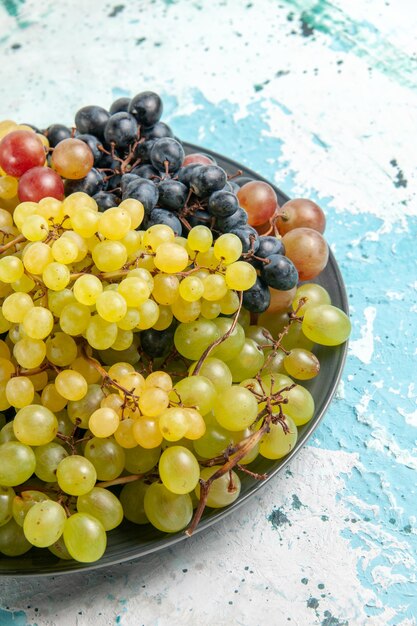 Vista frontal de uvas frescas coloridas frutas suculentas e maduras na superfície azul-clara