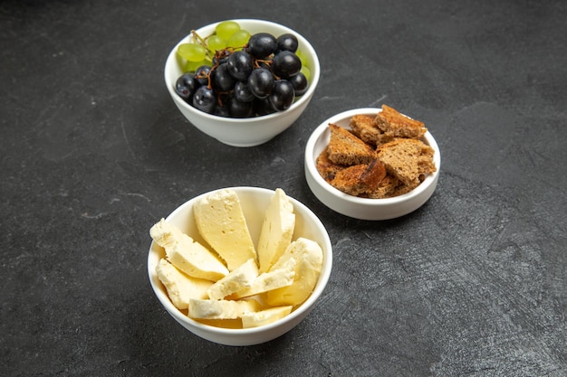 Vista frontal de uvas frescas com queijo branco e pão escuro fatiado na mesa escura prato de comida comida com frutas leite