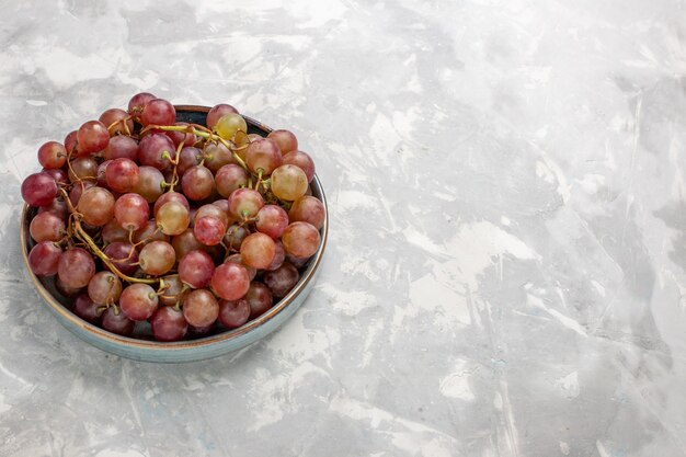 Vista frontal de uvas vermelhas frescas suculentas frutas suaves e doces na mesa branca clara