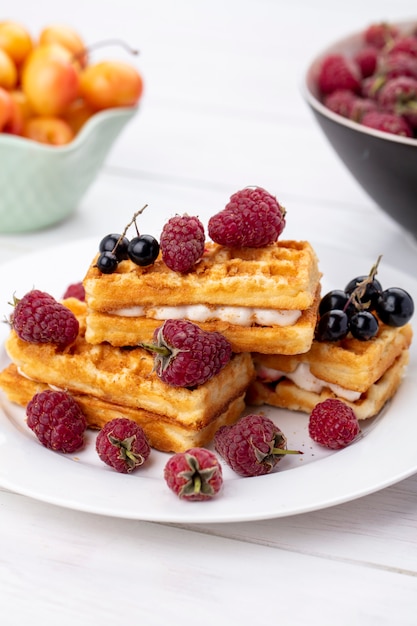 Vista frontal de waffles doces com framboesas em um prato sobre uma superfície branca