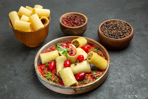 Vista frontal deliciosa refeição de massa italiana cozida com molho de tomate e temperos em fundo cinza.