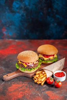 Vista frontal deliciosas batatas fritas com cheeseburgers em fundo escuro lanche prato fast-food jantar torrada hambúrguer