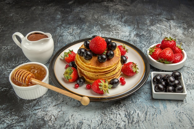 Vista frontal deliciosas panquecas com frutas frescas e mel no bolo doce de frutas superficiais