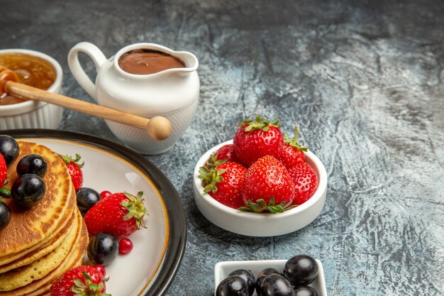 Vista frontal deliciosas panquecas com mel e frutas em um bolo de frutas de superfície clara