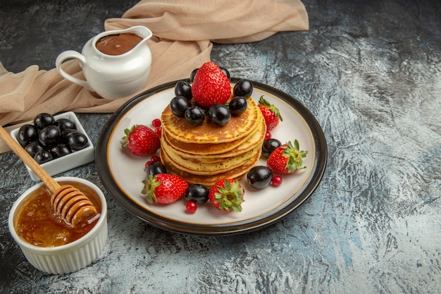 Vista frontal deliciosas panquecas com mel e frutas em um bolo de frutas doce de superfície clara