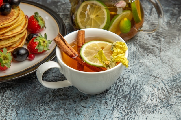 Vista frontal deliciosas panquecas com uma xícara de chá no bolo de frutas de chá de superfície clara