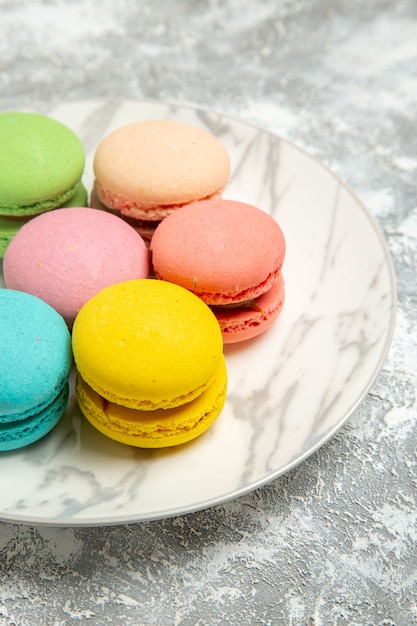 Vista frontal deliciosos macarons franceses bolos coloridos dentro do prato na mesa branca bolo biscoito de açúcar biscoitos de torta doce