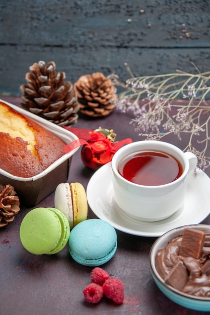 Vista frontal deliciosos macarons franceses com chocolate e uma xícara de chá no fundo escuro chá bebida torta biscoito bolo biscoito