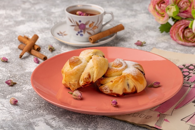 Vista frontal deliciosos pastéis com recheio dentro do prato junto com chá e canela na mesa branca, bolo de açúcar doce assar massa