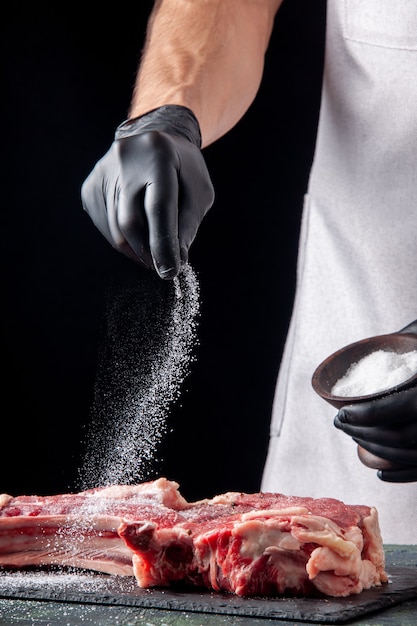Foto grátis vista frontal do açougueiro salgando carne em superfície escura