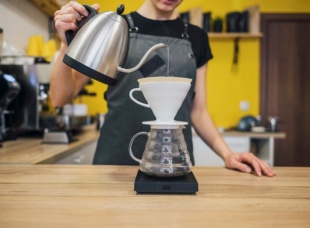 Vista frontal do barista feminino derramando água quente sobre o filtro de café