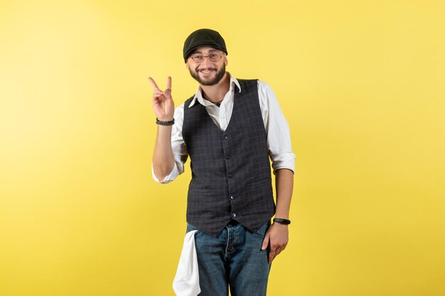 Vista frontal do barman sorrindo e mostrando o sinal da vitória na parede amarela modelo bebida trabalho trabalho clube noite masculina