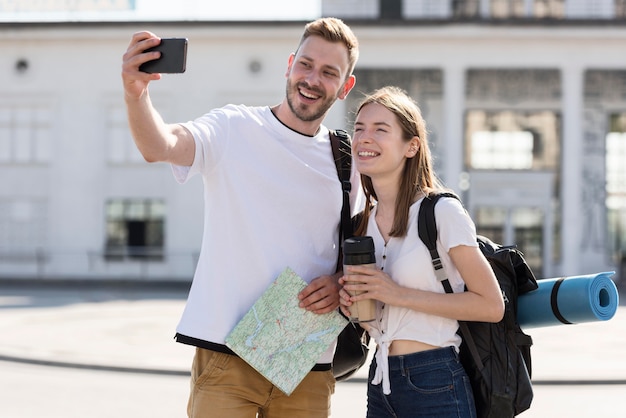Vista frontal do casal de turistas ao ar livre com mochilas tomando selfie