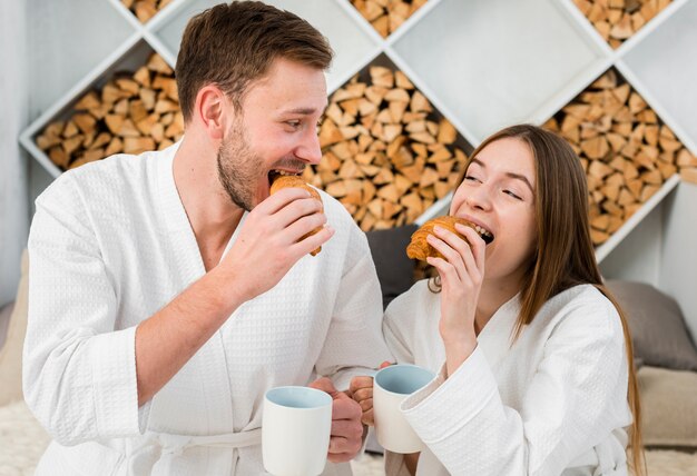 Vista frontal do casal sorridente comendo croissant