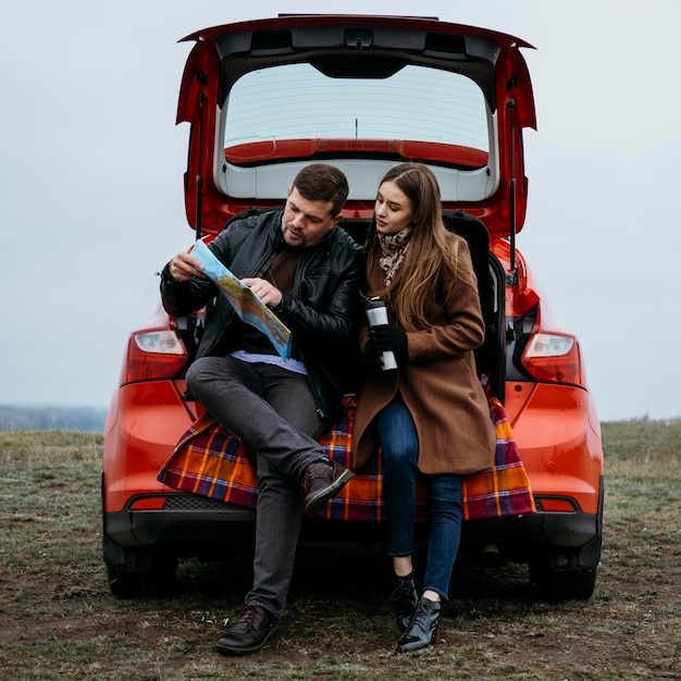Vista frontal do casal verificando um mapa no porta-malas do carro