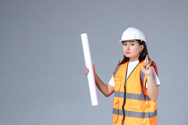 Vista frontal do construtor feminino com um pôster nas mãos na parede cinza