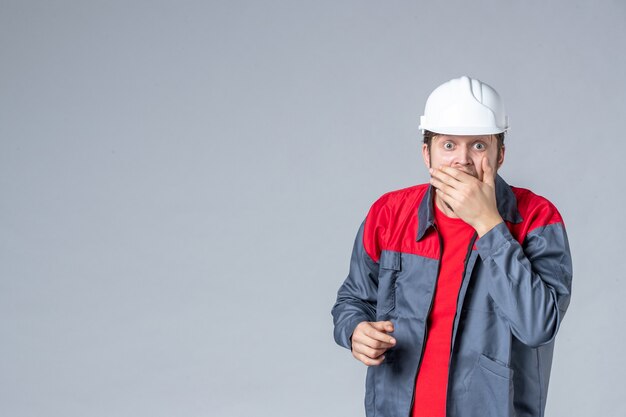 vista frontal do construtor masculino de uniforme e capacete em fundo cinza