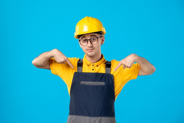 Vista frontal do construtor masculino de uniforme e capacete na parede azul