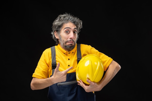 Vista frontal do construtor masculino em uniforme amarelo na parede preta