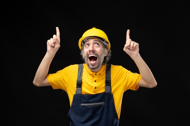 Vista frontal do construtor masculino em uniforme amarelo na parede preta