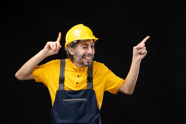 Vista frontal do construtor masculino em uniforme amarelo na parede preta