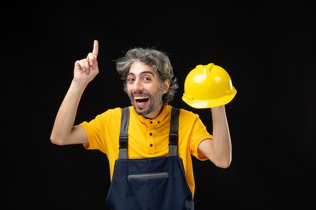 Vista frontal do construtor masculino em uniforme amarelo na parede preta