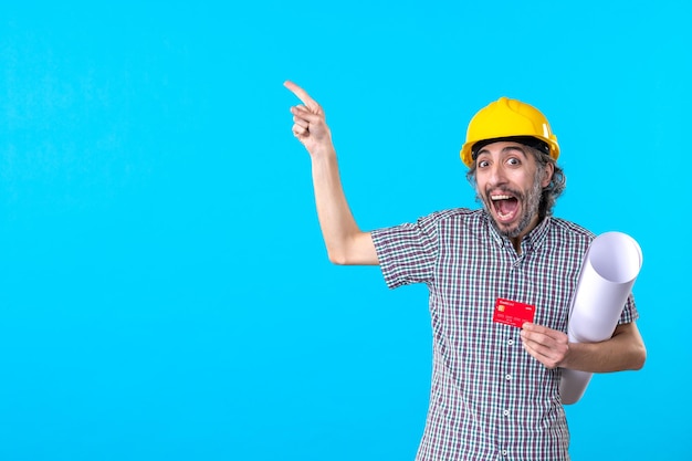 Vista frontal do construtor masculino segurando o plano e o cartão do banco sobre fundo azul projeto de dinheiro cor construtor trabalho de construção