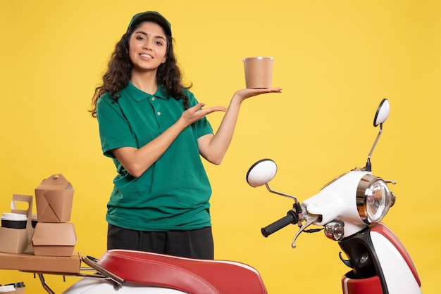 Vista frontal do correio feminino de uniforme verde com sobremesa no fundo amarelo cor de trabalho entrega de trabalho mulher serviço comida de trabalhador