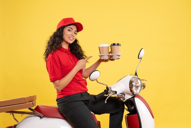 Vista frontal do correio feminino em bicicleta segurando xícaras de café no fundo amarelo trabalhador serviço uniforme trabalho mulher entrega trabalho