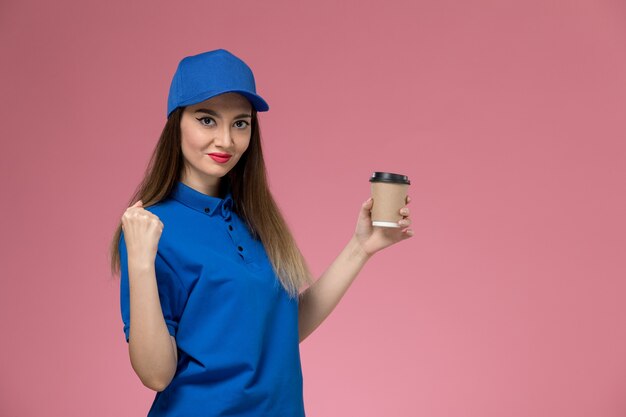 Vista frontal do correio feminino em uniforme azul e capa segurando a xícara de café de entrega na parede rosa trabalho menina mulher trabalhadora