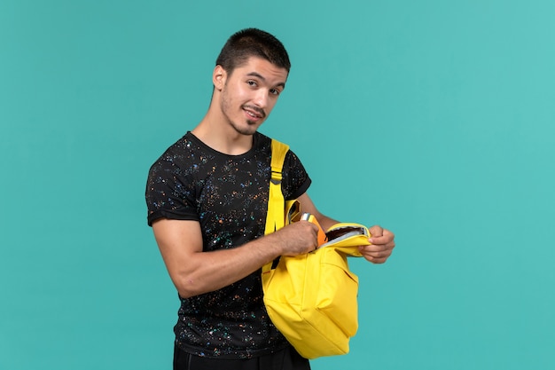 Foto grátis vista frontal do estudante do sexo masculino na mochila de camiseta amarela escura na parede azul claro