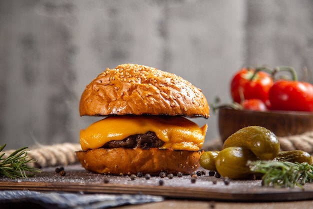 Vista frontal do hambúrguer de carne de queijo com pickles verdes e tomates na mesa de madeira