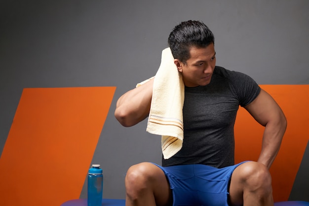 Vista frontal do homem atlético, limpando a cabeça com a toalha relaxante após o treino