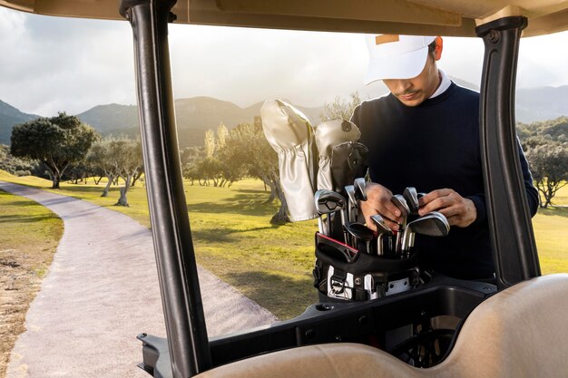 Vista frontal do homem com tacos de golfe ao lado do carrinho de golfe