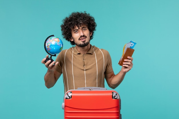 Foto grátis vista frontal do homem de férias segurando o globo e o ingresso em azul claro