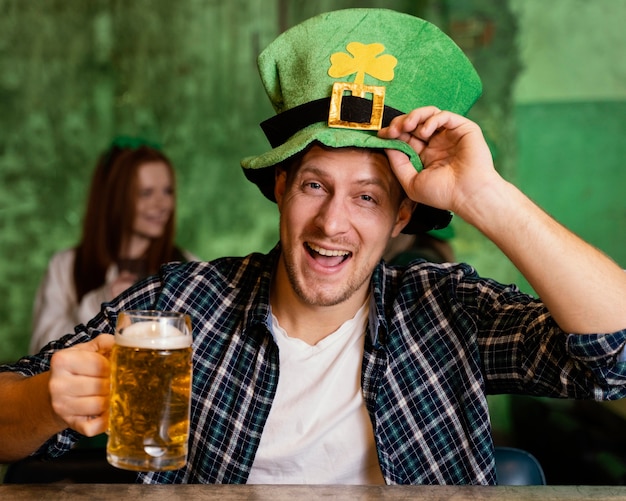 Vista frontal do homem feliz com chapéu comemorando st. dia de patrick com bebida