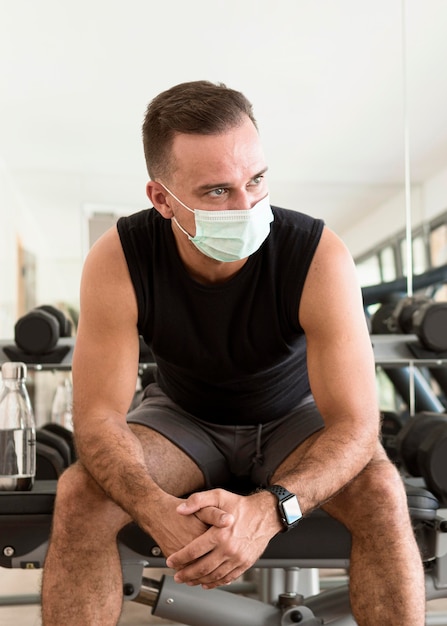 Vista frontal do homem na academia com máscara médica