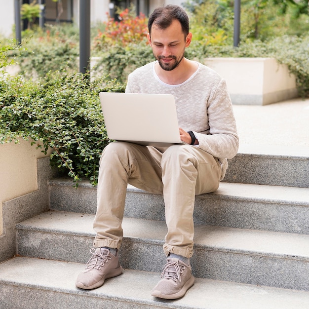 Vista frontal do homem trabalhando no laptop nos degraus