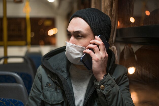 Vista frontal do homem vestindo máscara médica no ônibus e falando ao telefone