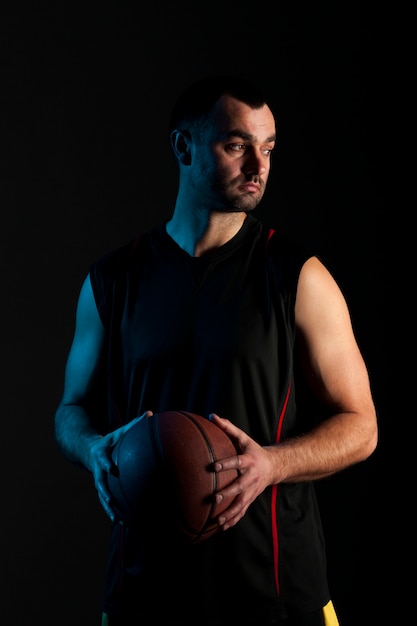 Vista frontal do jogador de basquete estóico segurando uma bola