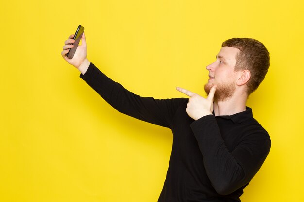 Vista frontal do jovem de camisa preta, tomando uma selfie com sorriso