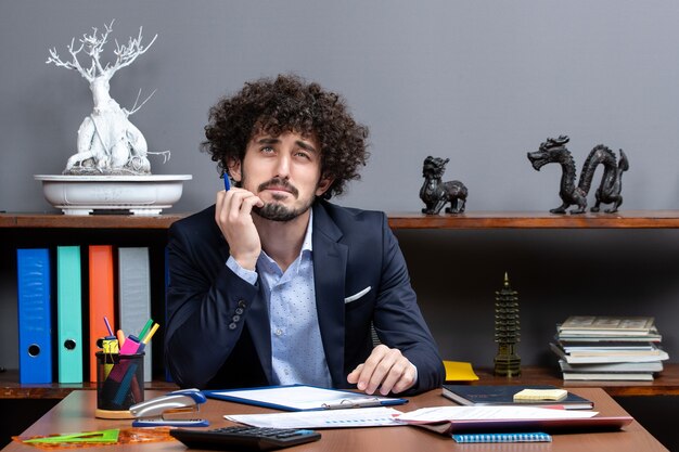 Vista frontal do jovem empresário pensativo sentado à mesa em um escritório moderno