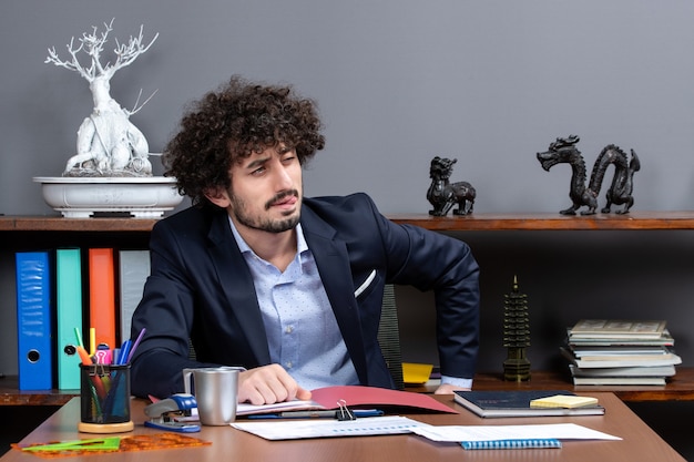 Foto grátis vista frontal do jovem empresário piscando os olhos, sentado à mesa no escritório